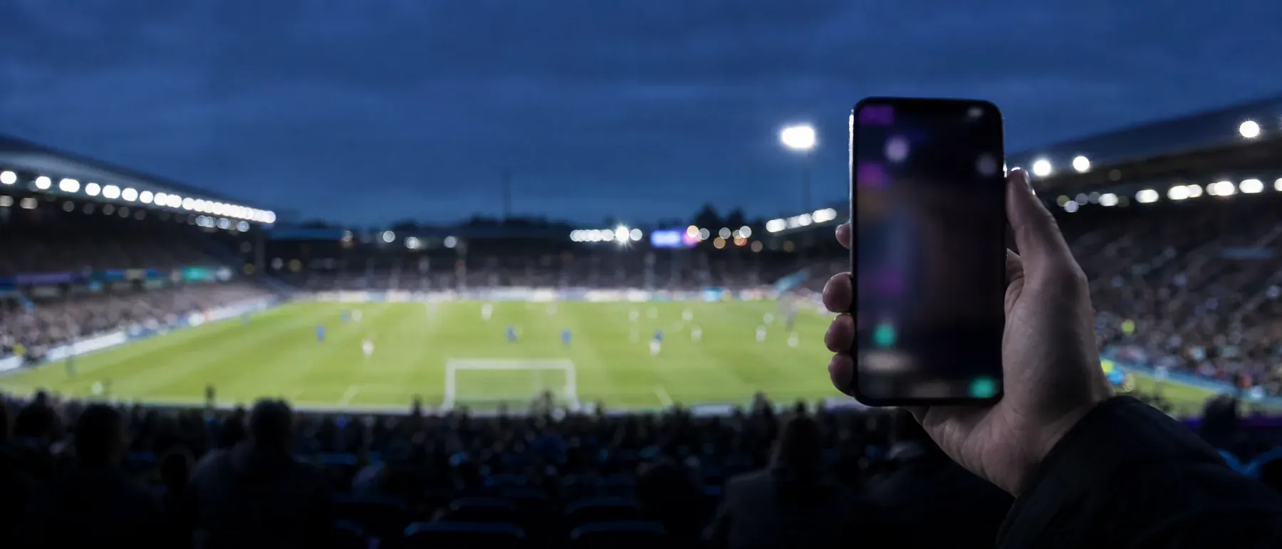 Smartphone tenu dans les tribunes d'un stade, pour une application paris sportifs